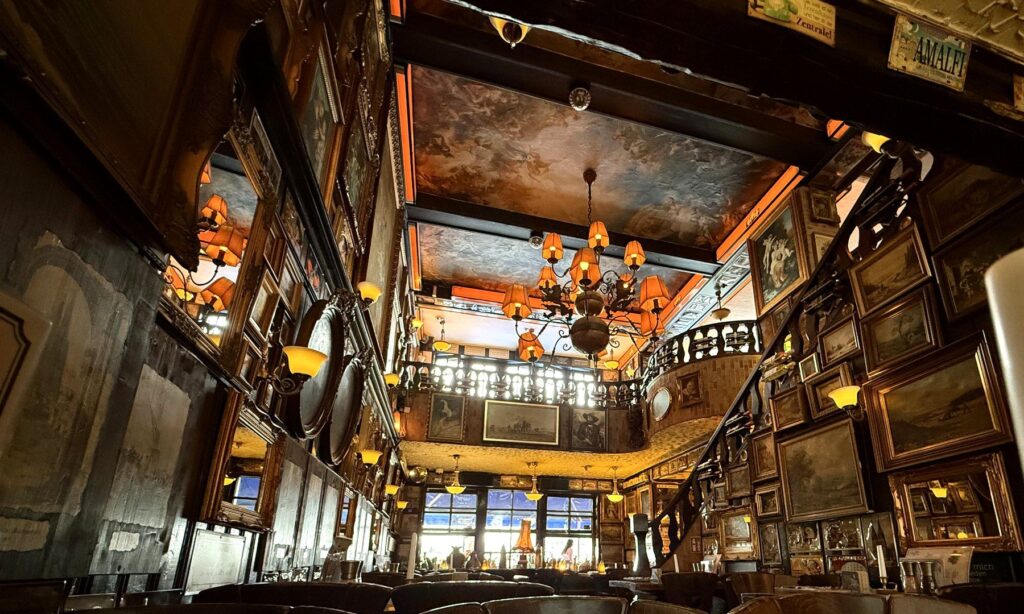 Historic dining room of the Löwenbräu Köln with painted ceiling, chandeliers and a wall of paintings