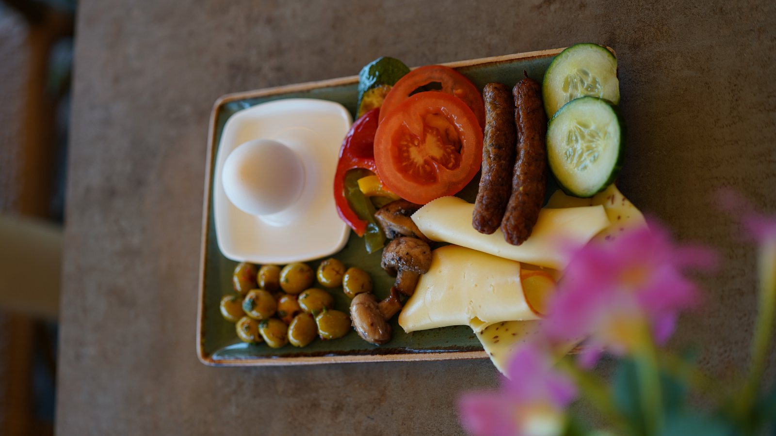 Frühstücksteller mit Oliven, Käse, Tomaten, Gurken, Ei und Würstchen